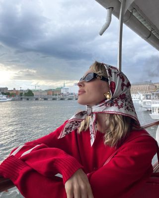 Woman in silk headscarf and red sweater on a boat.